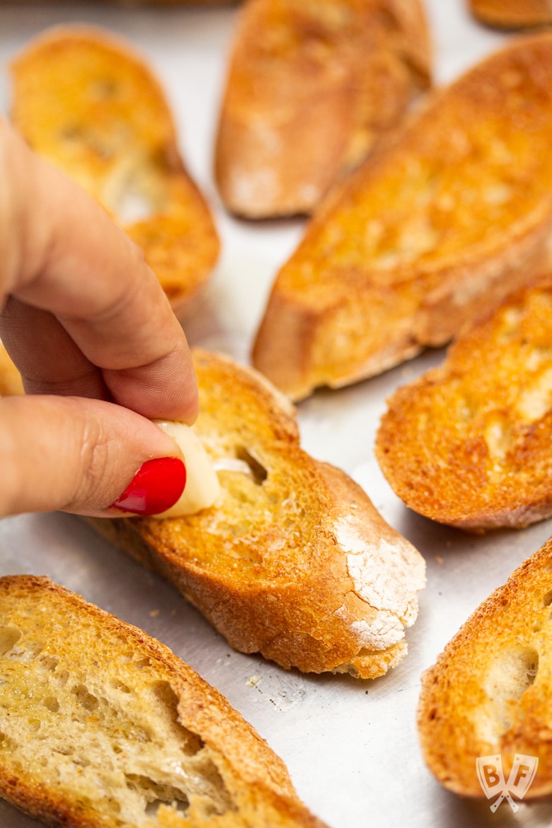 Rubbing a garlic clove onto toasted baguette slices for bruschetta