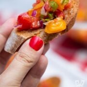 Hand holding a crostini topped with Italian tomato bruschetta
