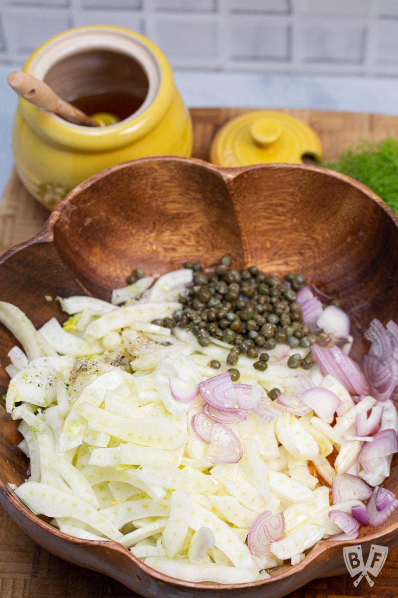 Fresh fennel, citrus, shallots, and capers in a large bowl.