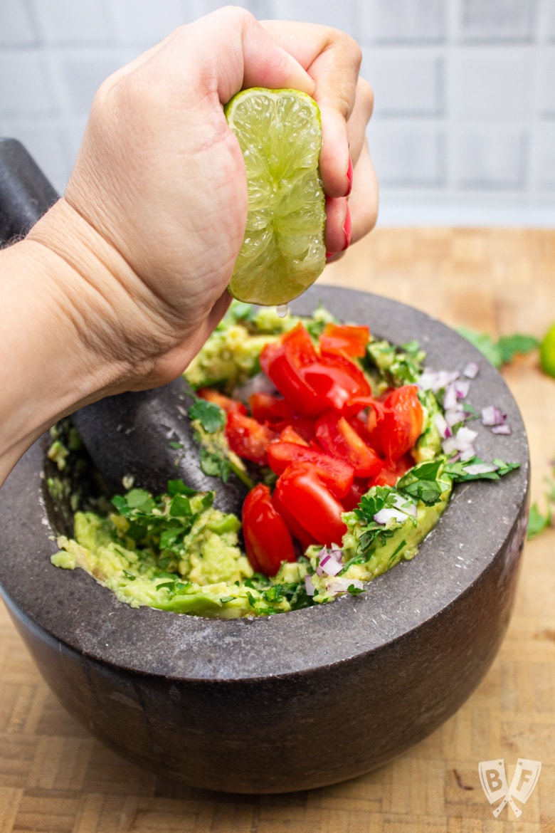 Squeezing a lime half into a mortar full of homemade guacamole.