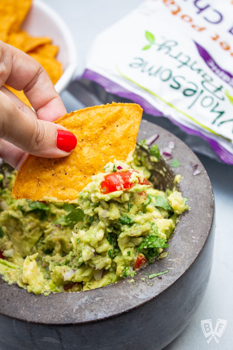 Scooping guacamole with a tortilla chip.