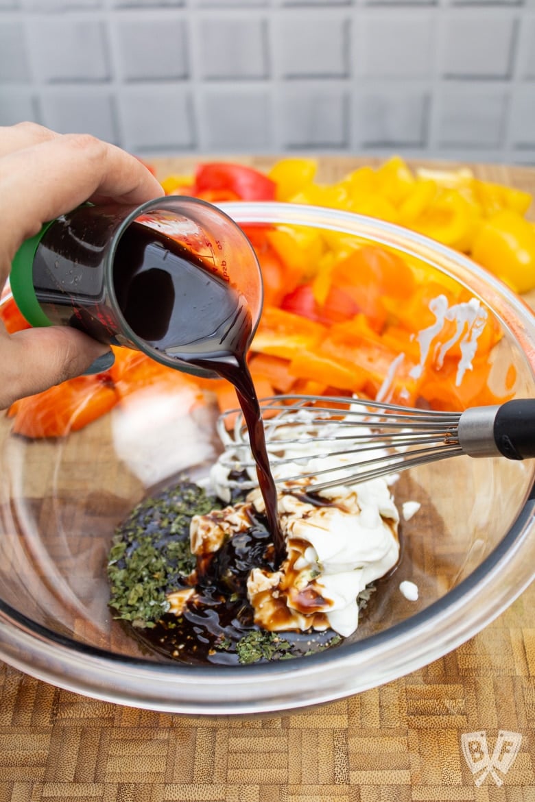 Adding balsamic vinegar to a bowl of ingredients to make vinaigrette.
