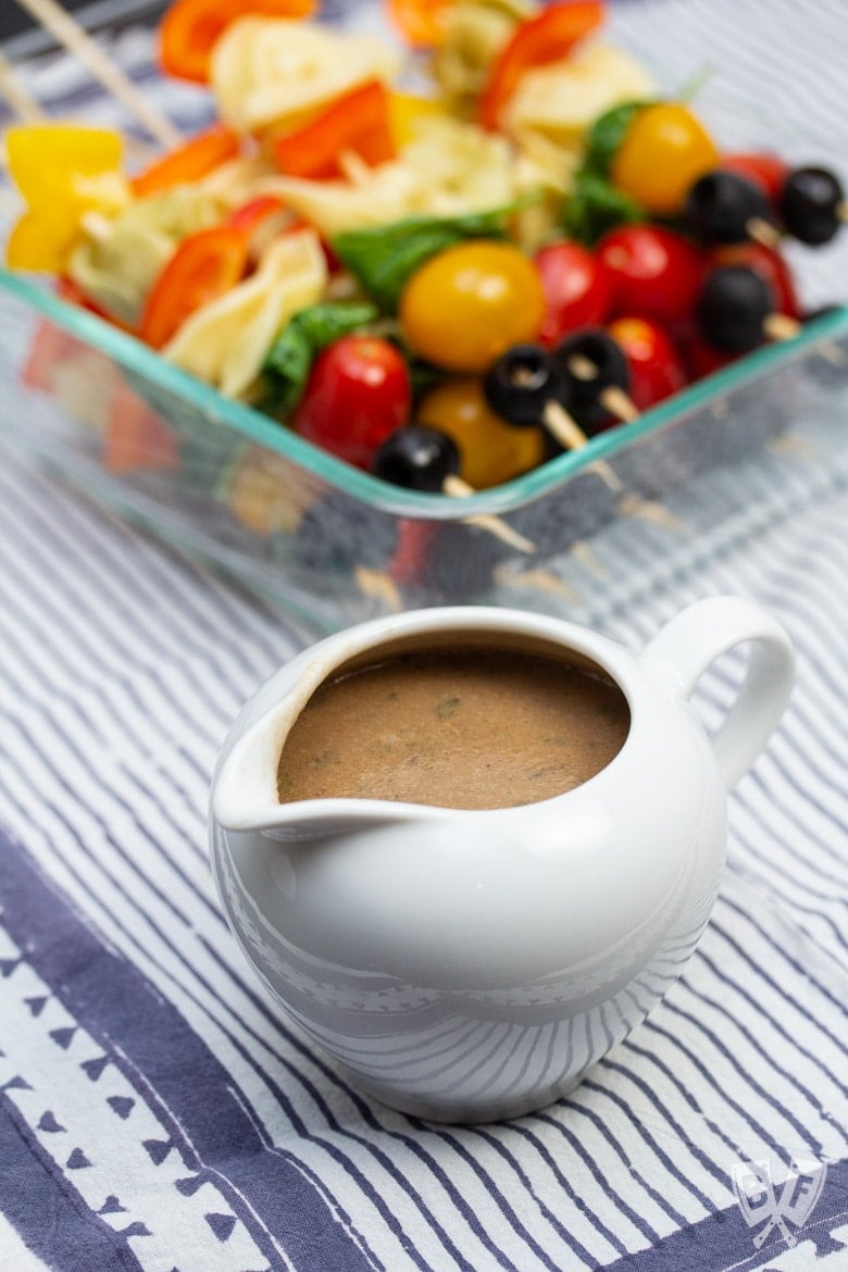 A platter of pasta salad skewers with a container of creamy balsamic vinaigrette.
