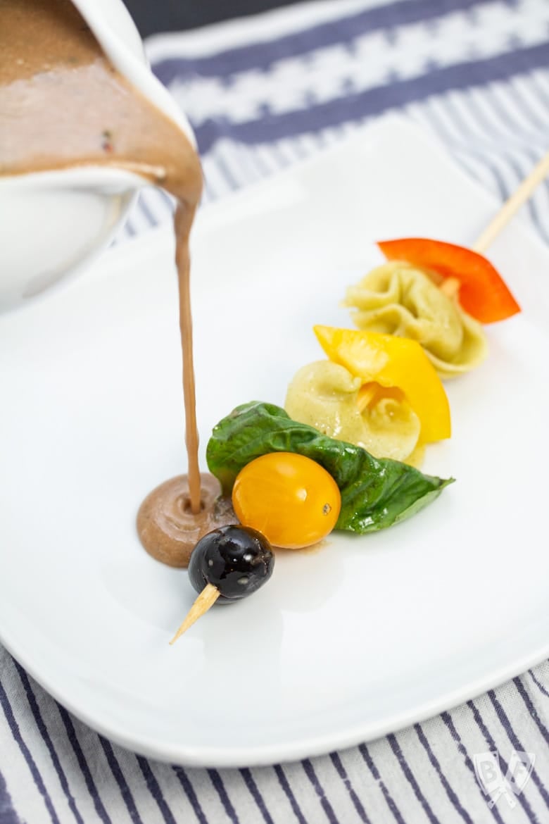 Drizzling creamy balsamic vinaigrette over a pasta salad skewer.