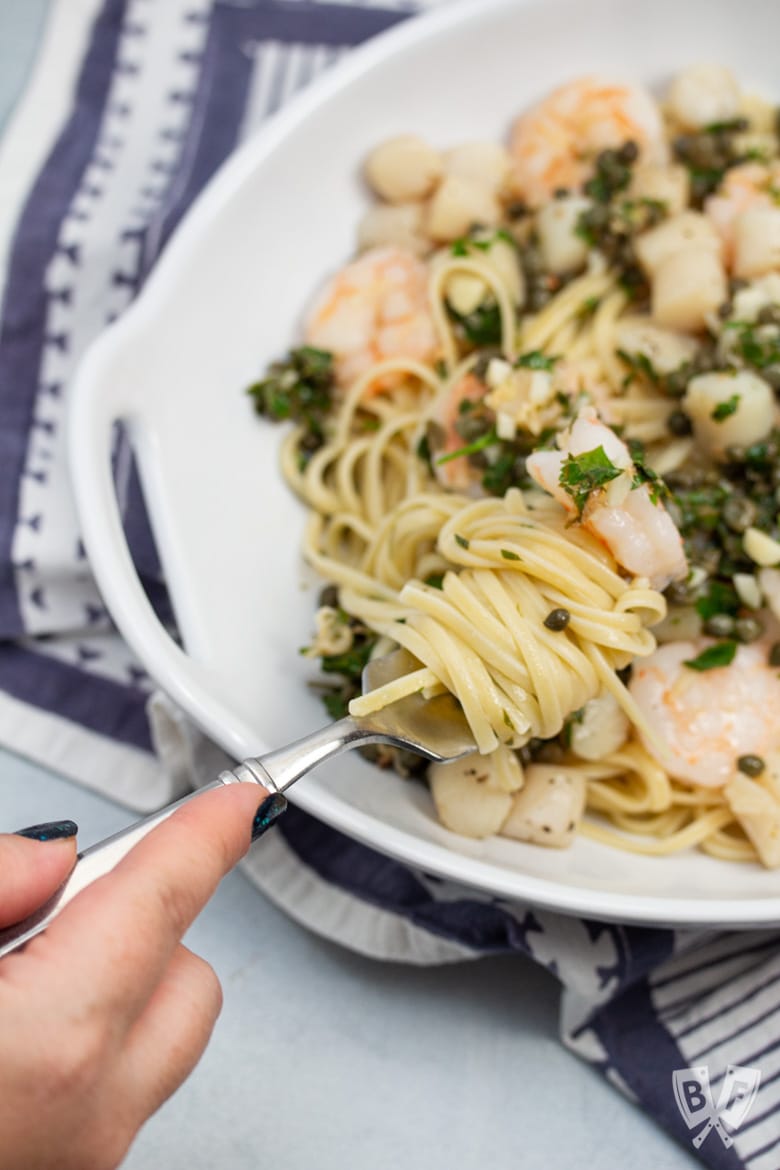 Fork twirling linguine in a bowl with shrimp and scallops.