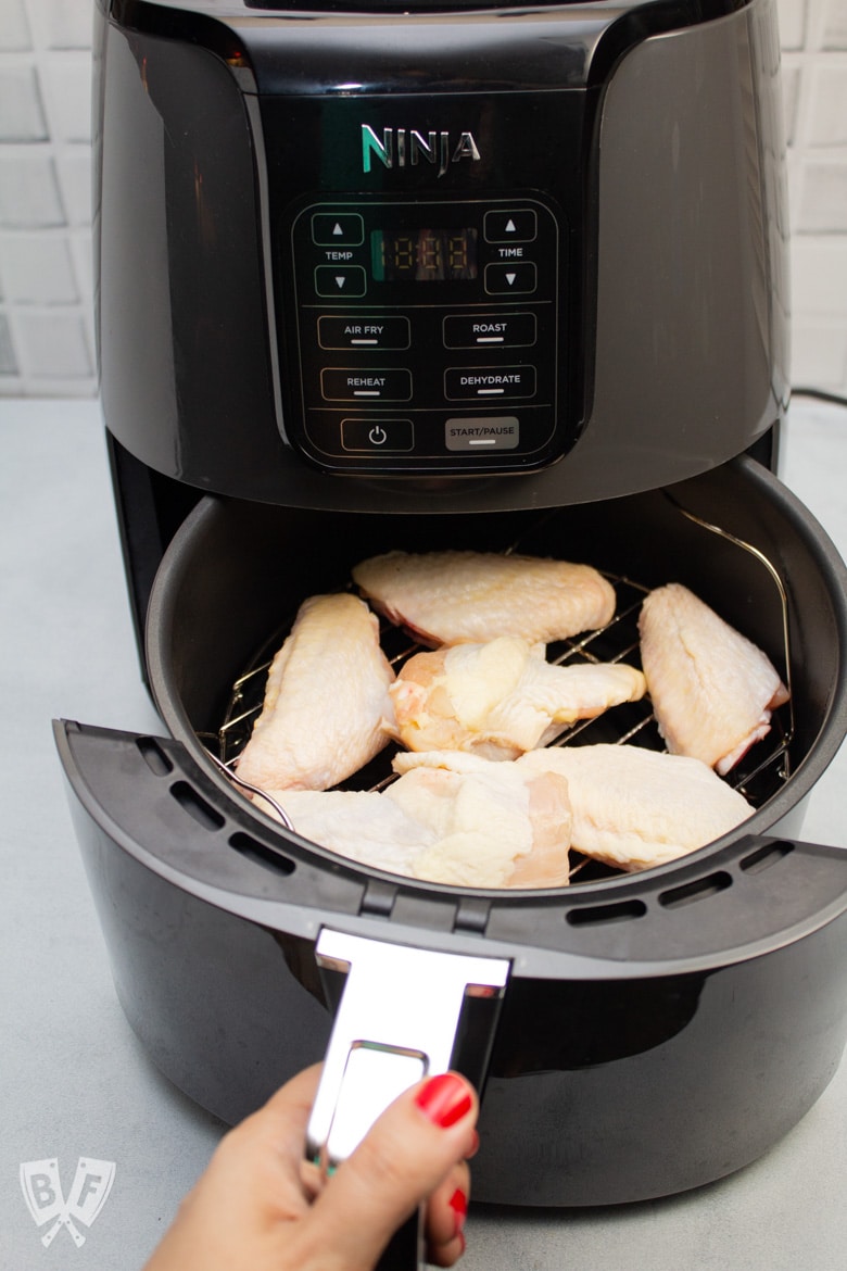 Air fryer tray with raw chicken wings on the rack