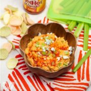 Buffalo chickpea dip in a bowl with wing sauce, celery sticks, and veggie chips alongside