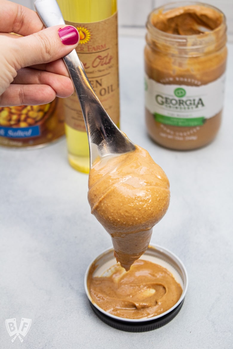 Spoon of creamy peanut butter with peanut products in the background