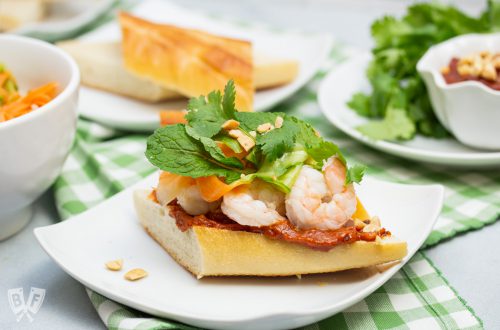 Vietnamese shrimp sandwich on a plate piled with pickled veggies, fresh herbs and peanut sauce.