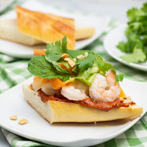 Vietnamese shrimp sandwich on a plate piled with pickled veggies, fresh herbs and peanut sauce.
