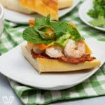 Vietnamese shrimp sandwich on a plate piled with pickled veggies, fresh herbs and peanut sauce.