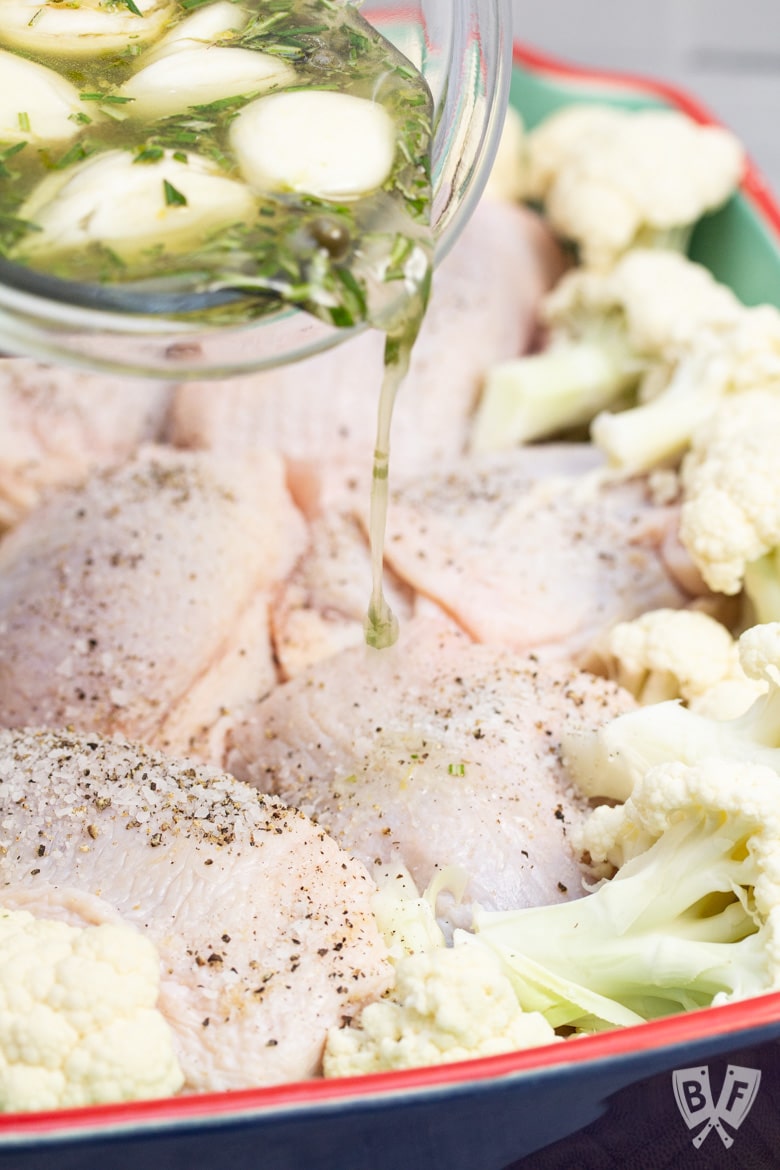 Drizzling rosemary lemon garlic oil over chicken thighs and cauliflower