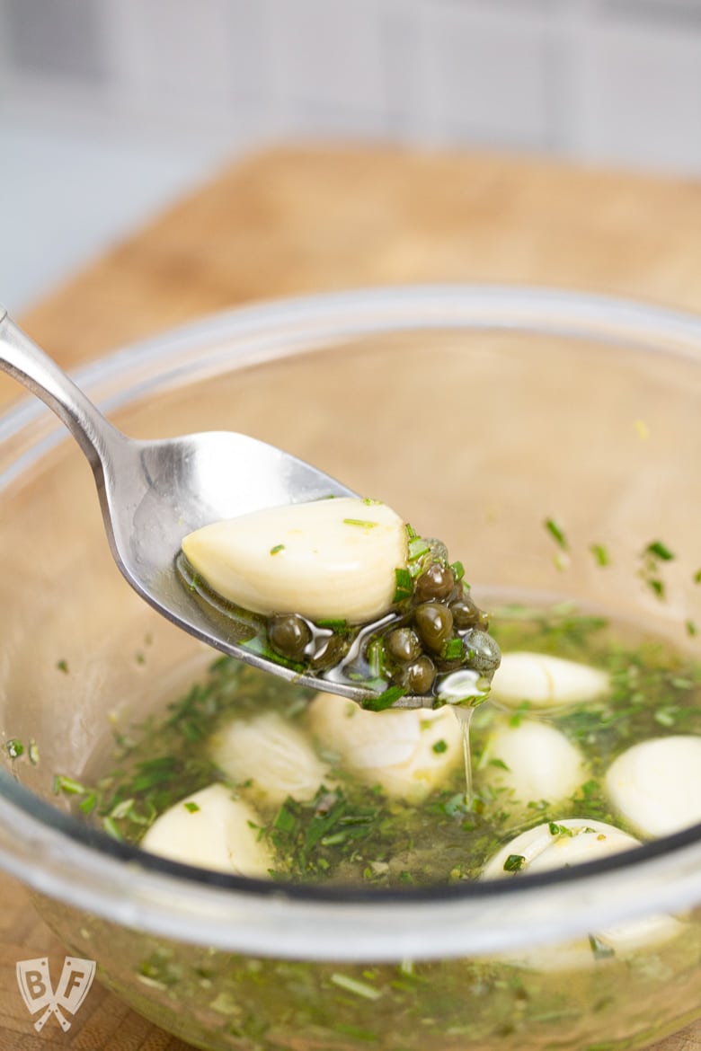 Spoon lifting a mixture of garlic, rosemary, and olive oil from a bowl