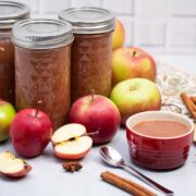 Jars of applesauce surrounded by apples and whole spices.