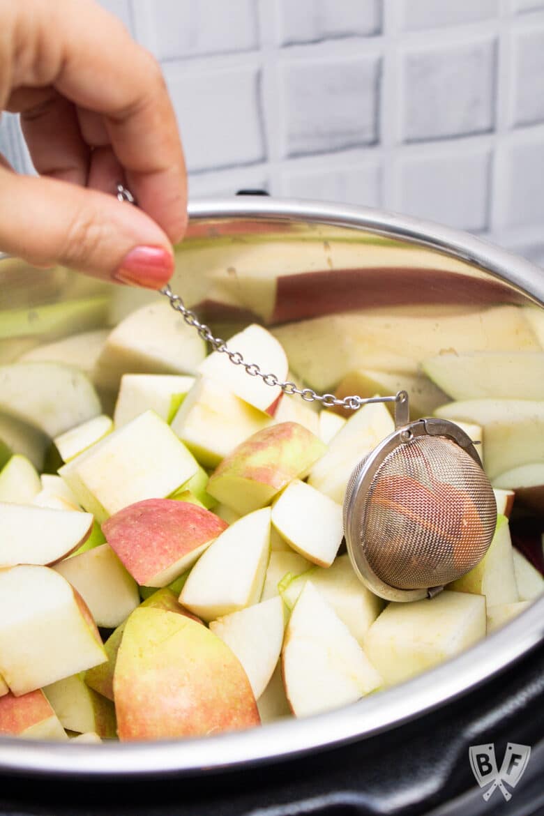 A tea ball being used as a sachet to add spices to a pot of apples for homemade applesauce.