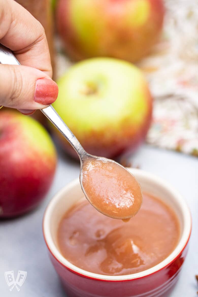 A spoonful of homemade mulled cider applesauce with apples in the background.