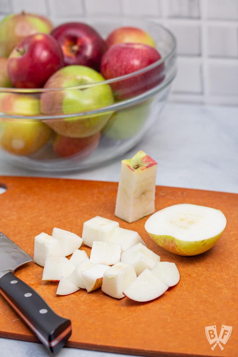 Apples being cut on a cutting board with a bowl of apples in the background.