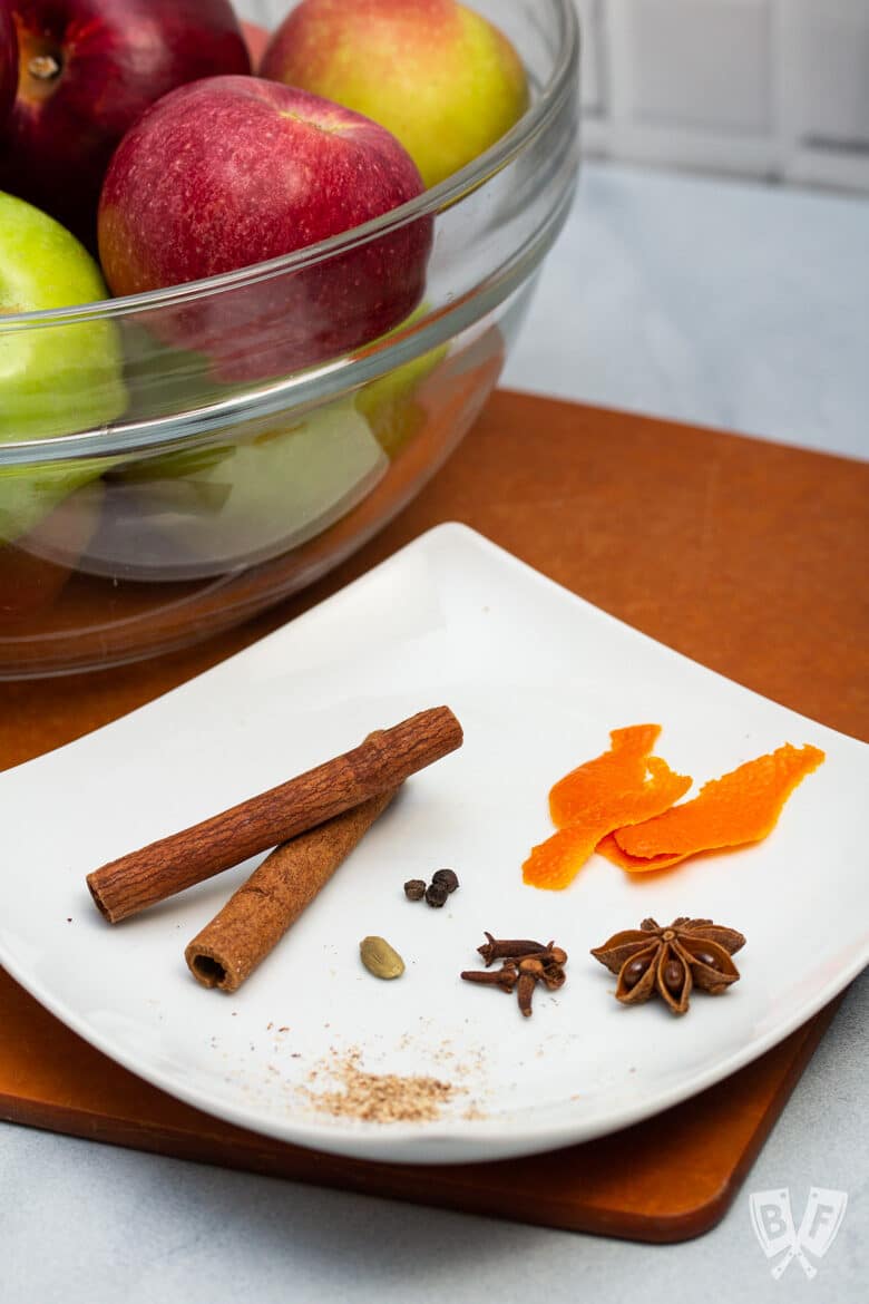 Mulling spices on a plate in front of a bowl of apples.