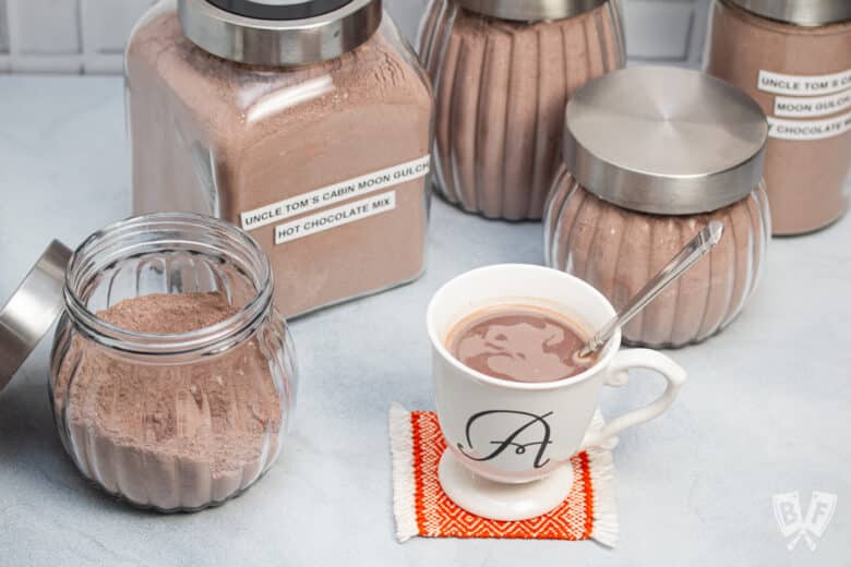 Jars of hot cocoa mix with a mug of brewed hot chocolate.