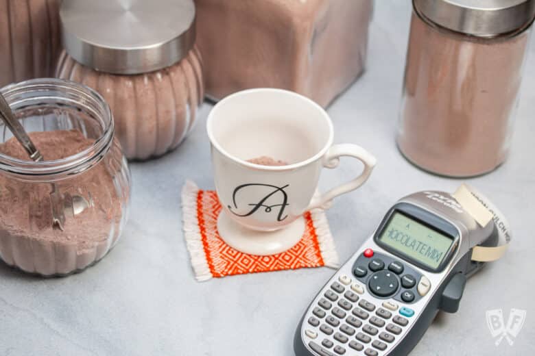 Label maker printing labels for homemade hot cocoa mix with jars surrounding.