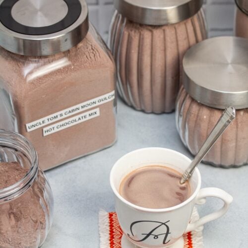 An assortment of jars of hot cocoa mix with a mug of hot chocolate up front.