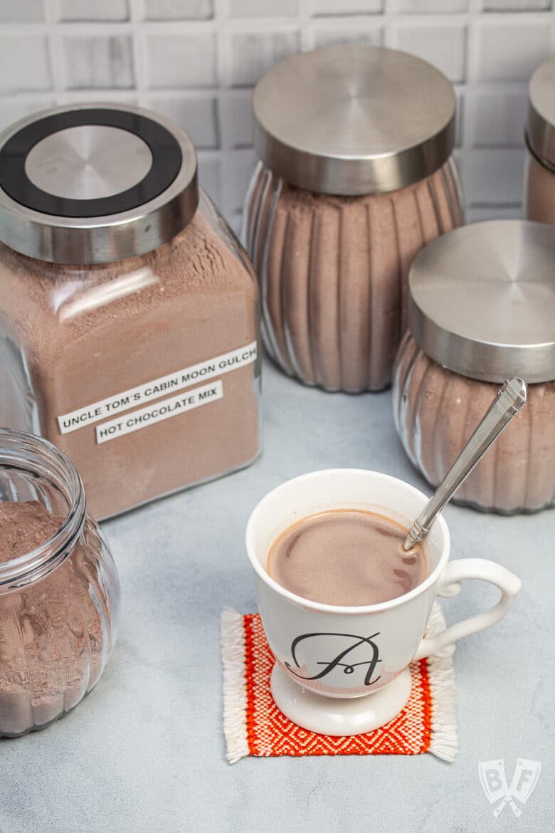 An assortment of jars of hot cocoa mix with a mug of hot chocolate up front.