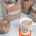 Homemade hot cocoa in a mug surrounded by jars of hot cocoa mix.