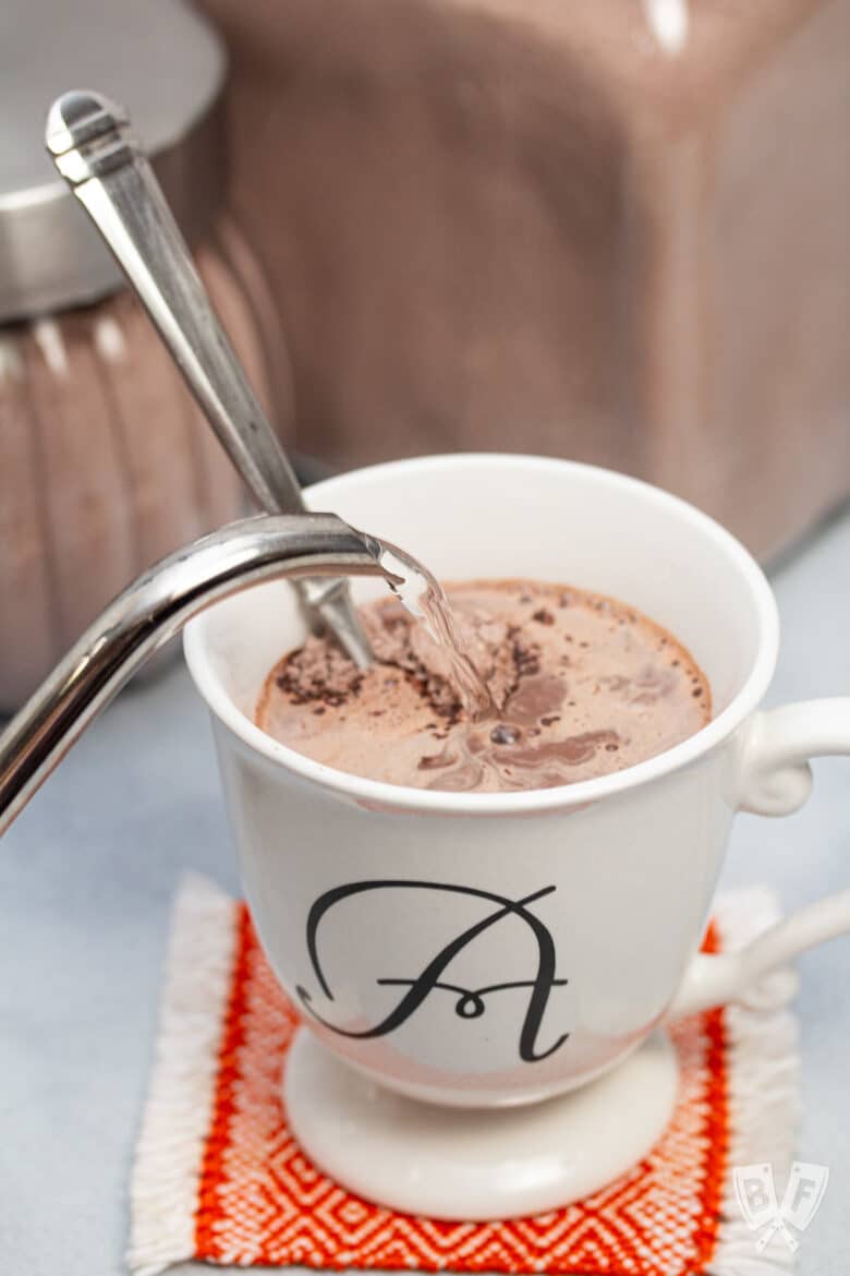 Pouring hot water into a mug of hot chocolate mix.