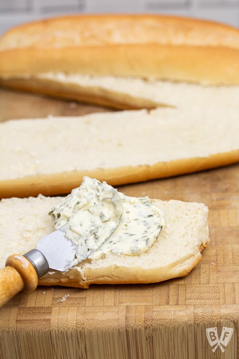 Spreading garlic herb butter on bread to make garlic bread.