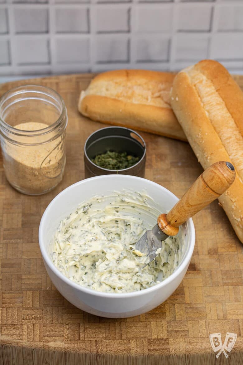 Overhead view of a bowl of garlic herb butter with bread and ingredients alongside.