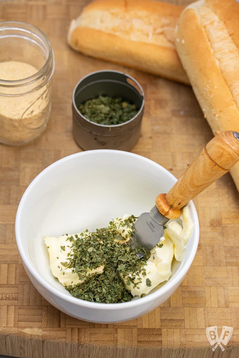 Overhead view of a bowl of garlic herb butter with bread in the background.
