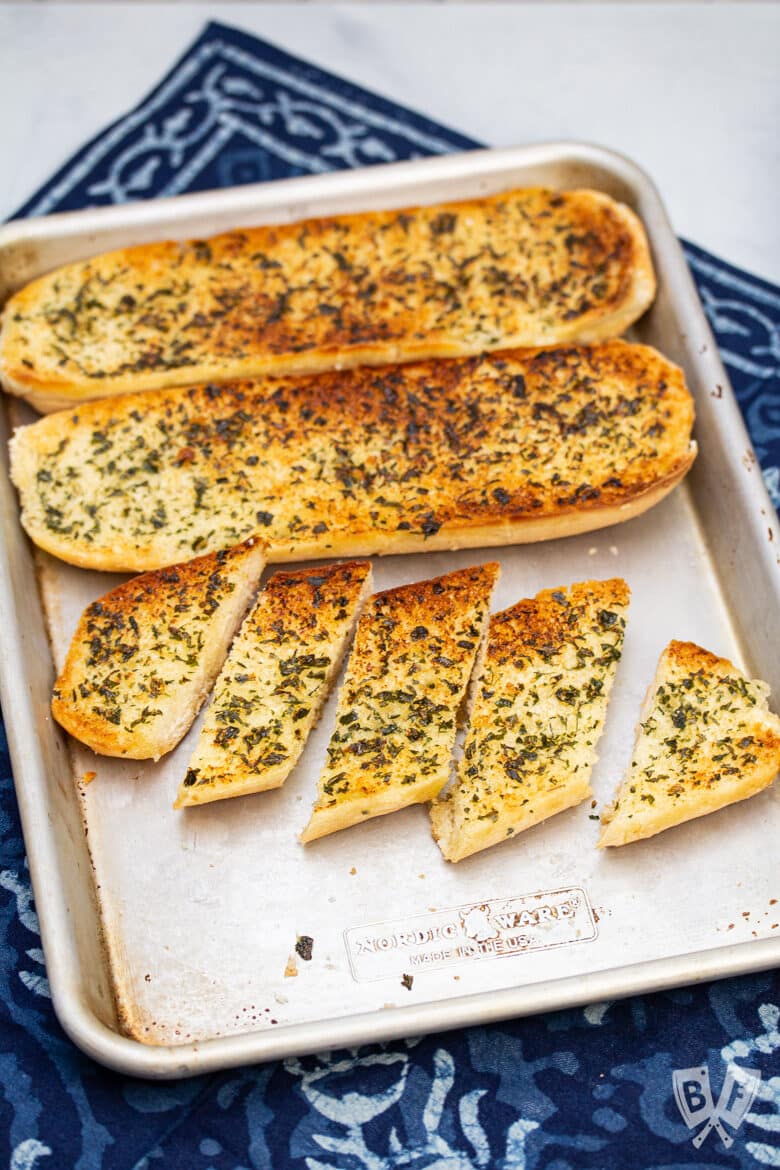 Overhead view of a tray of garlic bread with some cut into smaller pieces.