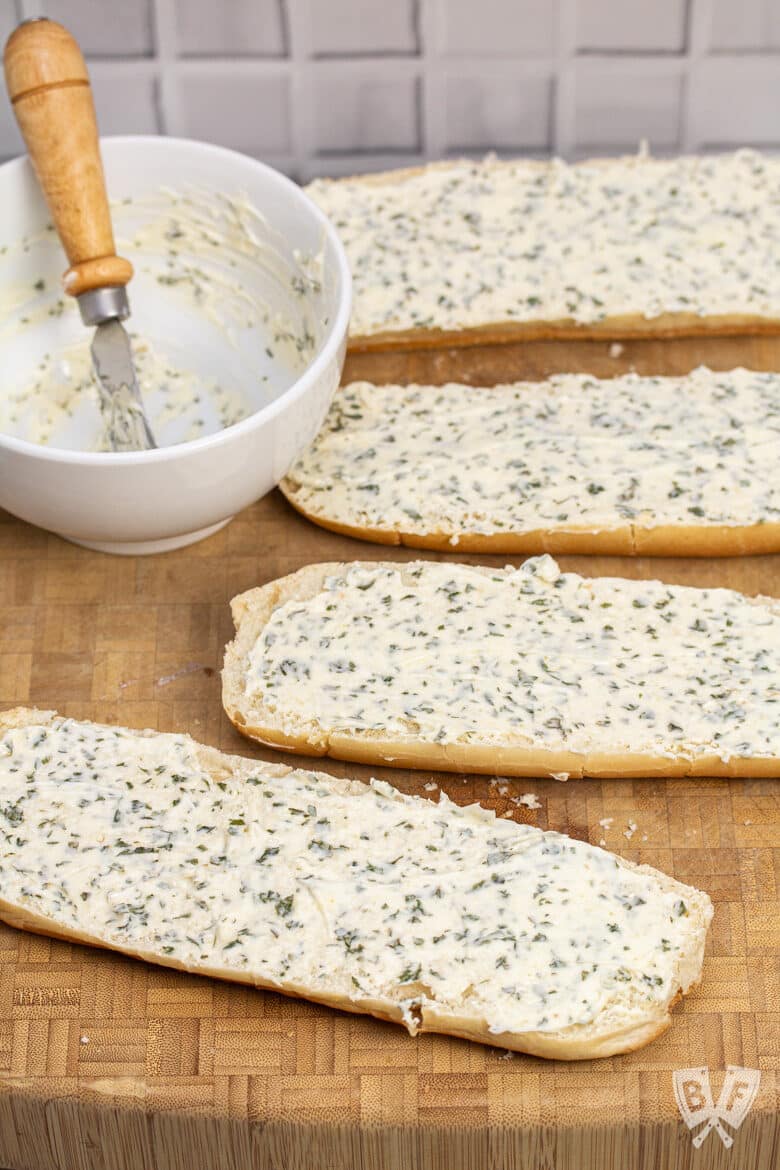 Overhead view of bread slathered with garlic herb butter ready to cook to make garlic bread.