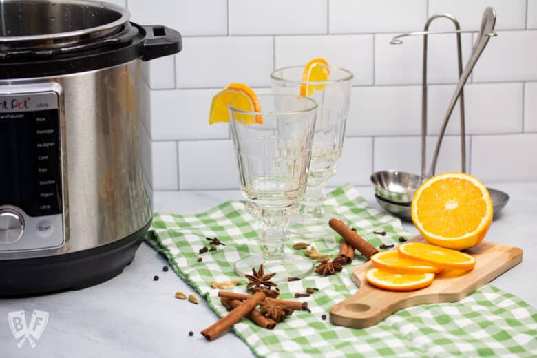 Instant Pot next to winter spices, sliced oranges, and glasses for red wine.