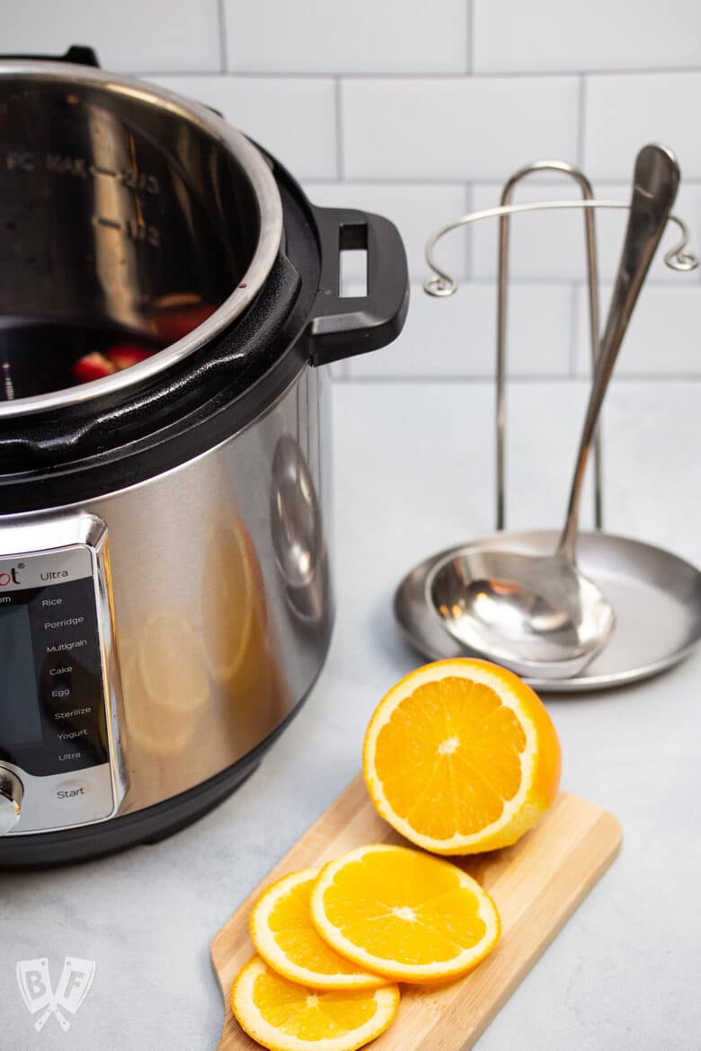 Instant Pot with mulled wine next to a sliced orange and a ladle.