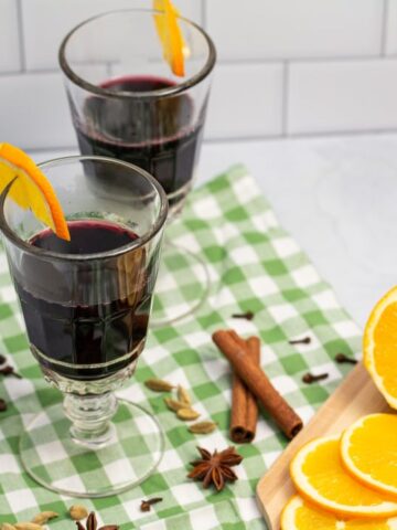 Two glasses of mulled wine surrounded by spices and orange slices.
