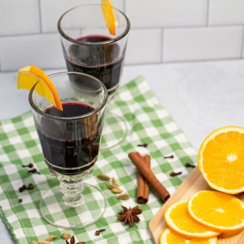 Two glasses of mulled wine surrounded by spices and orange slices.