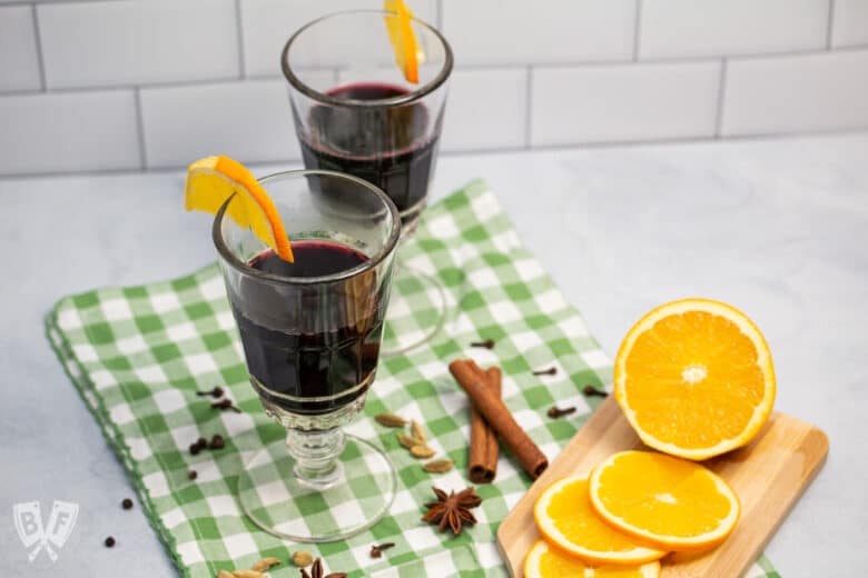 Two glasses of mulled wine surrounded by spices and orange slices.