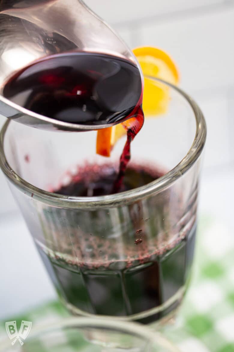 Ladling mulled wine into a glass garnished with an orange slice.