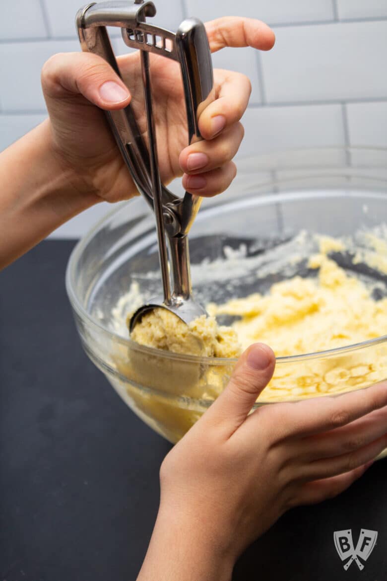 Scooping sweet corn muffin batter from a bowl.