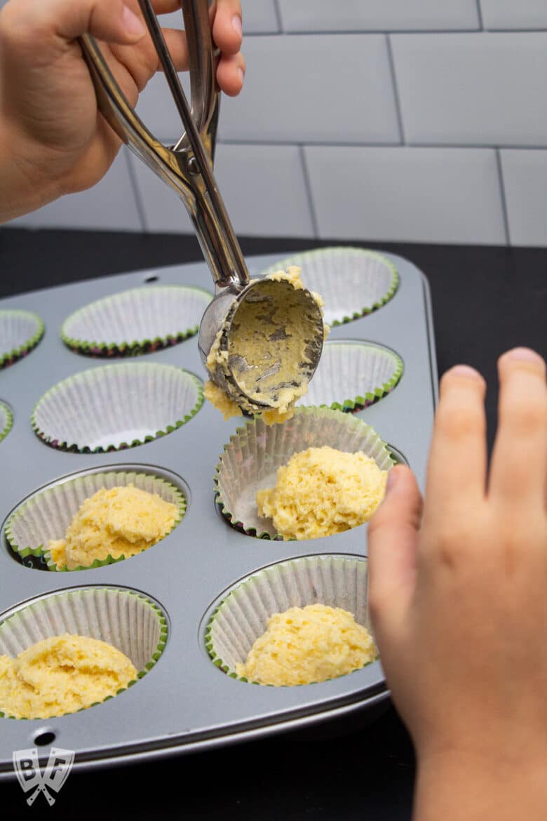 Dishing out sweet corn muffin batter into a lined muffin tin.