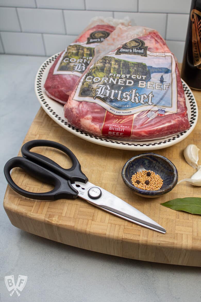 Kitchen scissors on a cutting board with corned beef brisket, spices, and garlic.