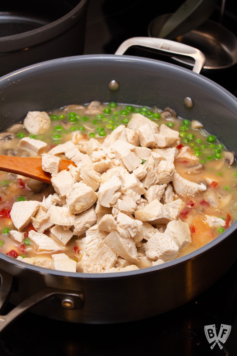 Stirring cubed chicken breast into a pan of veggies and sauce.