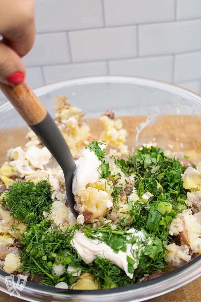 Stirring mayonnaise and herbs into potato salad.