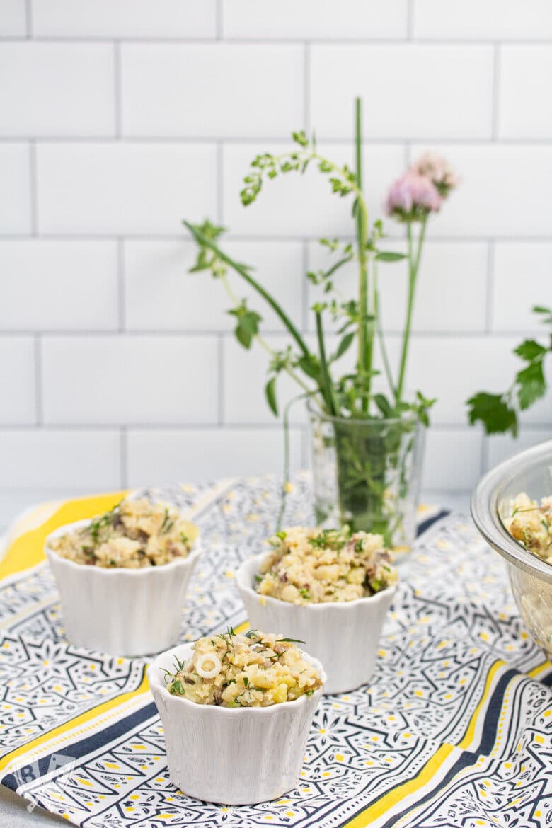 Ramekins of potato salad with fresh herbs in the background.