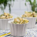 3 containers of potato salad with fresh herbs in the background.