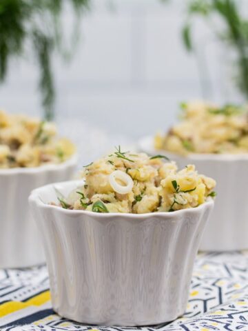3 containers of potato salad with fresh herbs in the background.