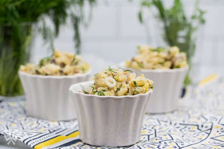 3 containers of potato salad with fresh herbs in the background.