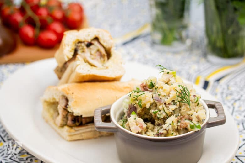 Herbed potato salad on a plate with a grilled chicken sandwich.