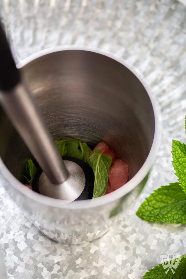 Muddling watermelon with fresh mint in a cocktail shaker.